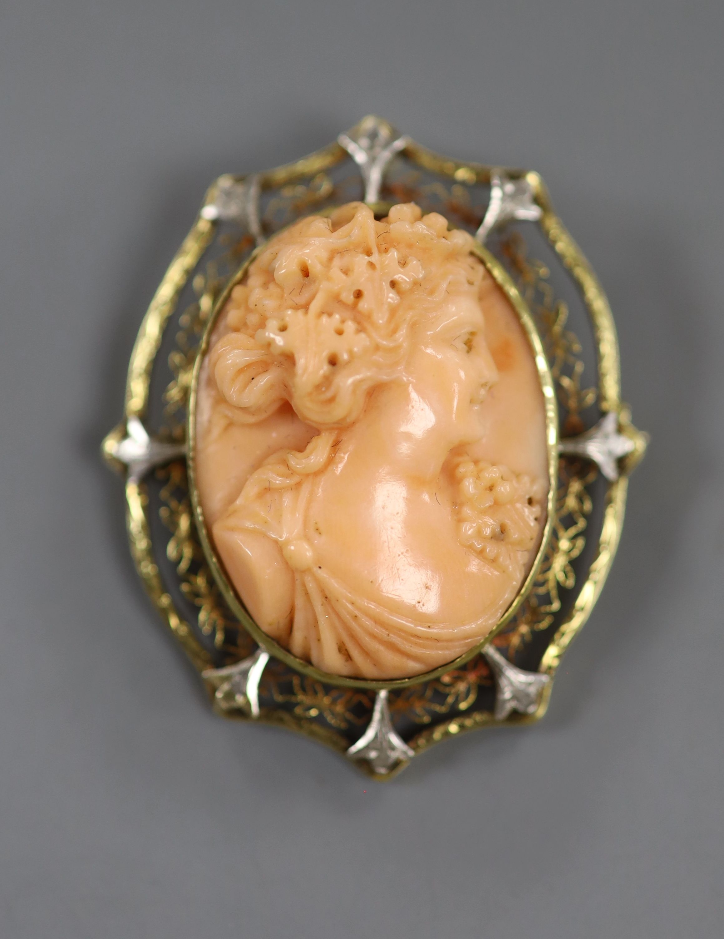 An early 20th century yellow and white metal mounted oval coral pendant brooch, carved with the bust of a lady to sinister